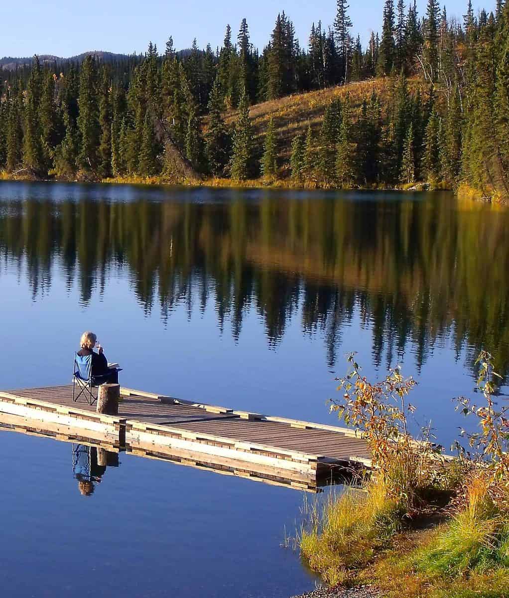 A woman sitting on a dock beside the calm waters of a lake