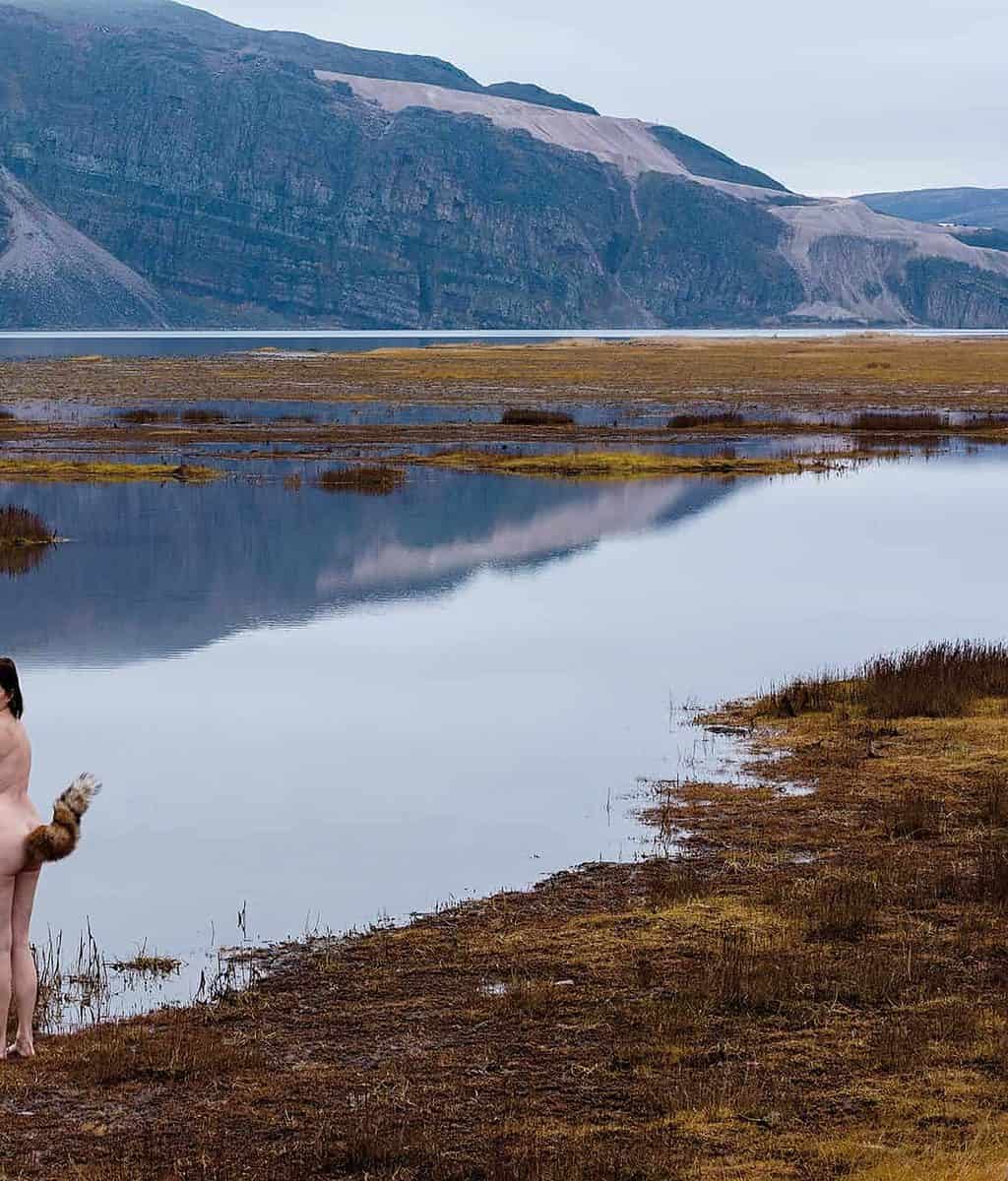 A naked woman standing by a lake in the mountains