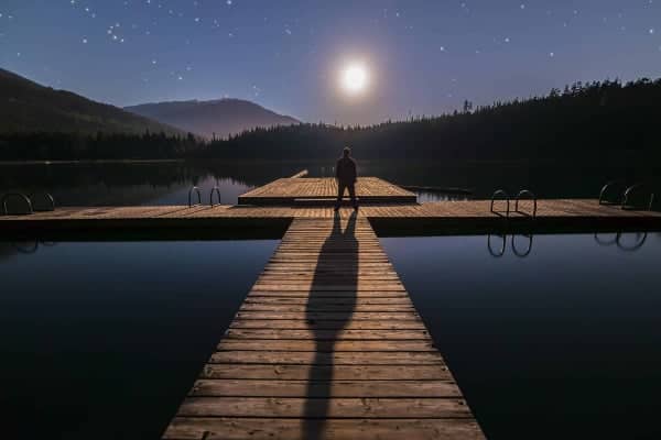 A man standing on a dock under a full moon