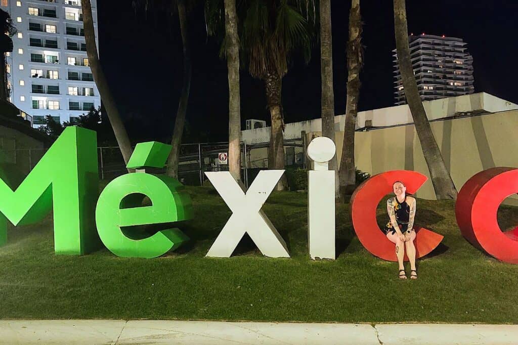 A woman stands beside a large sign for Mexico