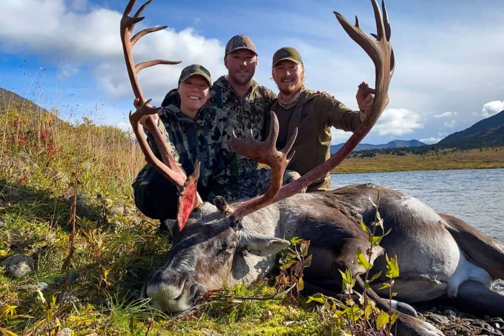 Three people pose with a harvested caribou