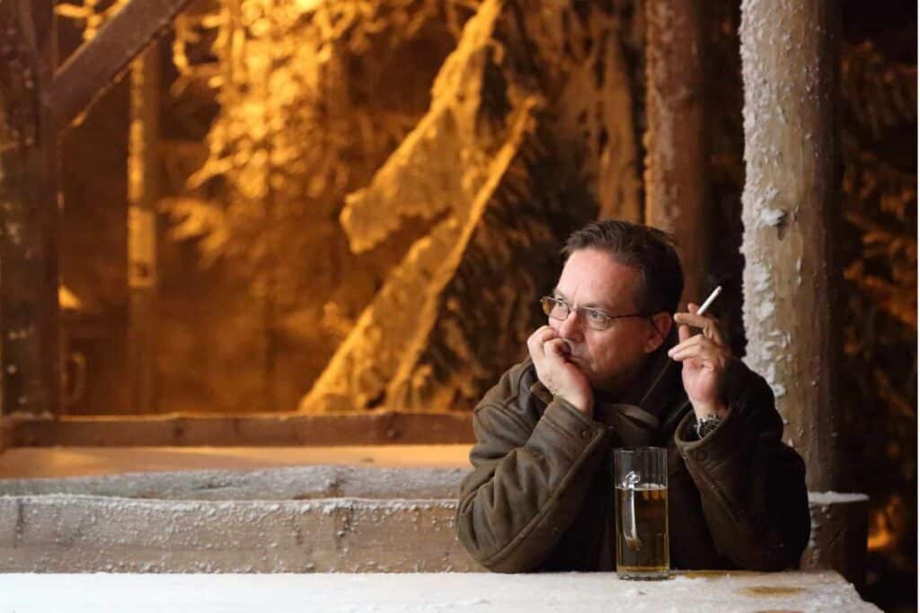 A man sitting alone with a cigarette and beer