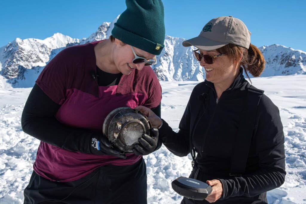 Two women examine artifacts in the snow