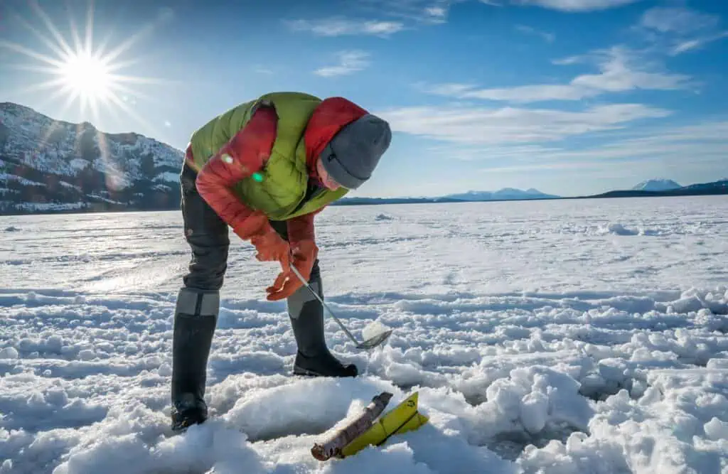A woman clearing ice from a fishing hole